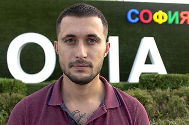 Photo of Daniel with green shrubs behind him and part of sofia sign