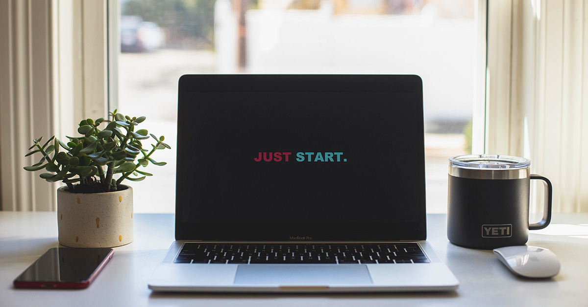 Laptop on a table with a sign "Just start"