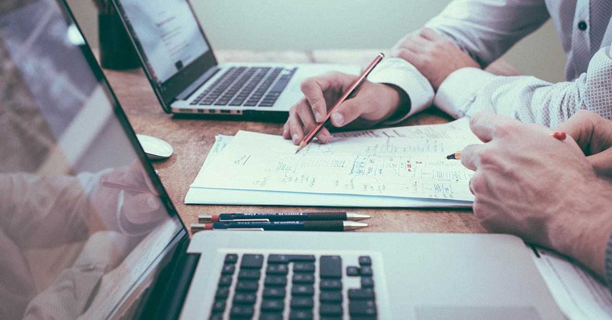 Two people planning a product strategy in front of two laptops and a list of paper.